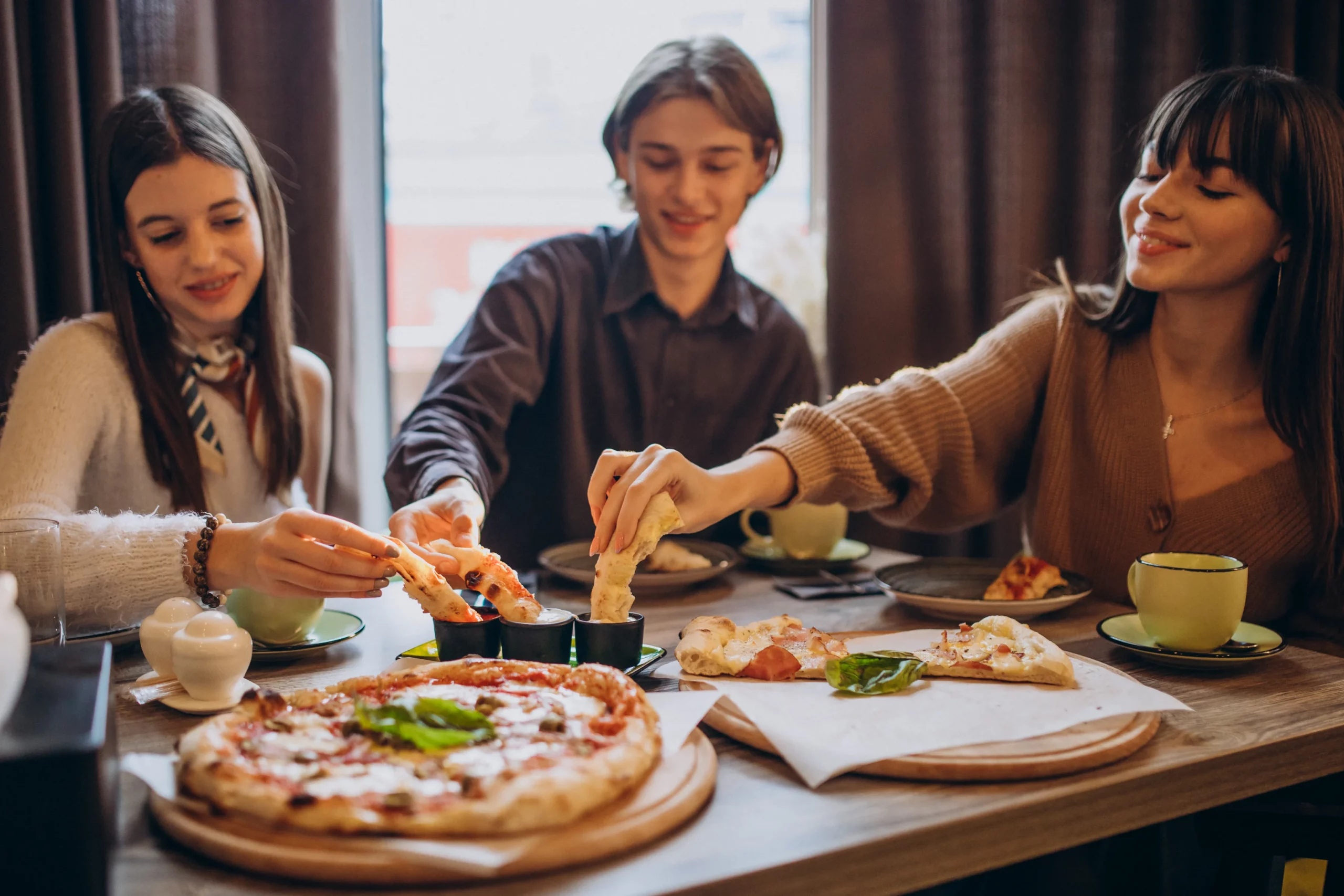 three friends together eating pizza cafe scaled